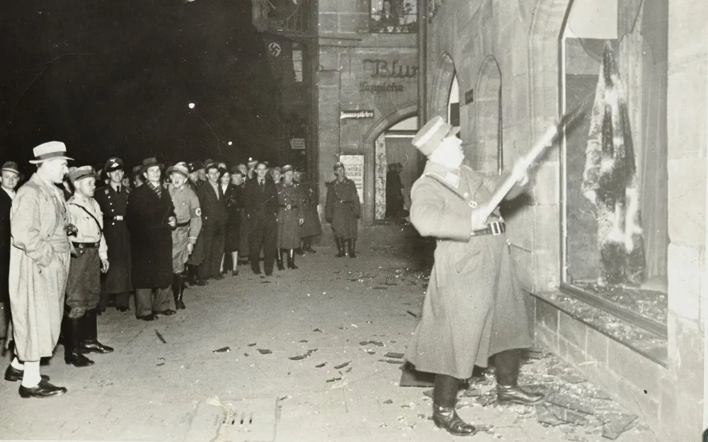 Nazis alemanes y civiles observan el saqueo de propiedades judías durante la Kristallnacht, probablemente en la ciudad de Fuerth, Alemania, el 10 de noviembre de 1938.